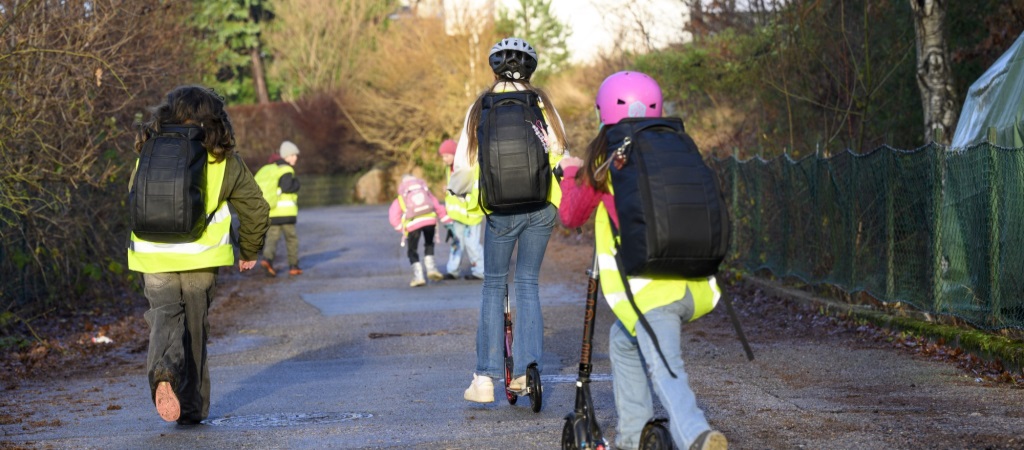 Barn som går til skolen på ben og sparkesykkel. De har på seg refleksvest